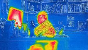 Red, green, yellow, blue thermal image of a man sitting in an office setting