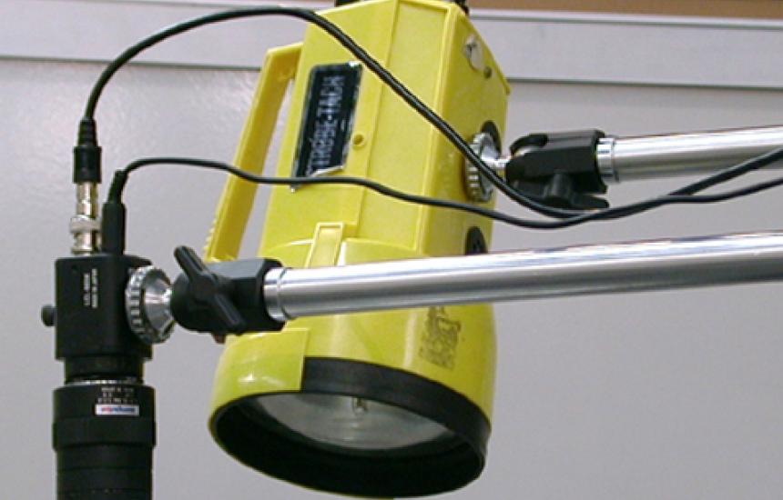A strobe light and a video camera are mounted directly above the glass object.