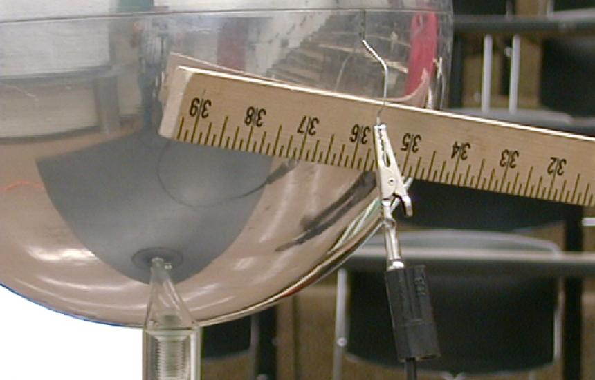 A meter stick is used to remove the ground wire from the metal sphere.
